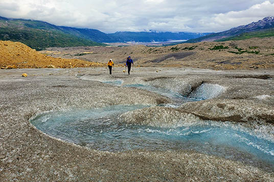 Alaskan hikers on a glacier with a clear glacial stream