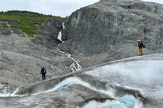 A hiker observes a waterfall from a glacier
