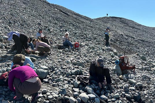 Hikers sit on rocks and put on their crampons