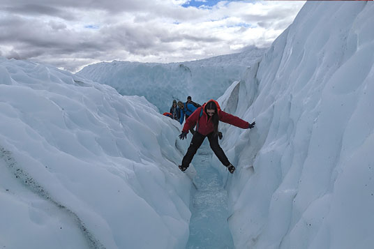 A hikers stems across a small glacial waterfall