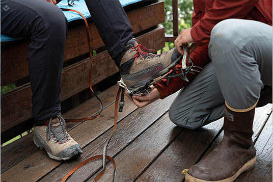 A guide kneels as he fits a crampon to a clients hiking boot