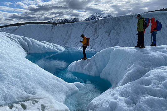 Hikers approach a brilliant blue glacial river