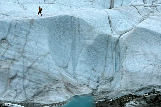 A hiker on above a tall wall on the Root Glacier in Alaska