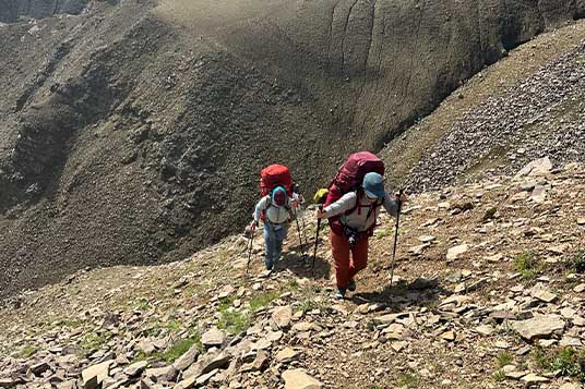Two backpackers walk uphill on steep scree