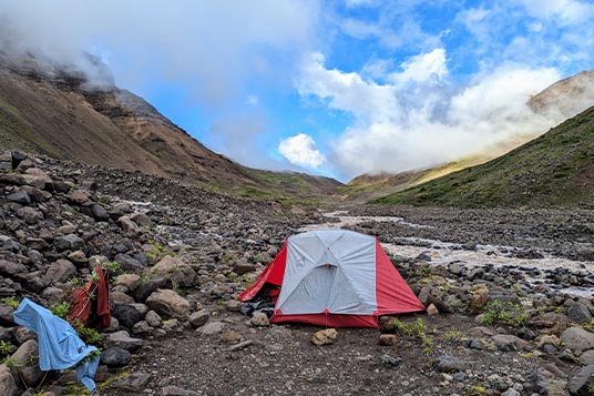 A tent set up on a rocky valley bottom