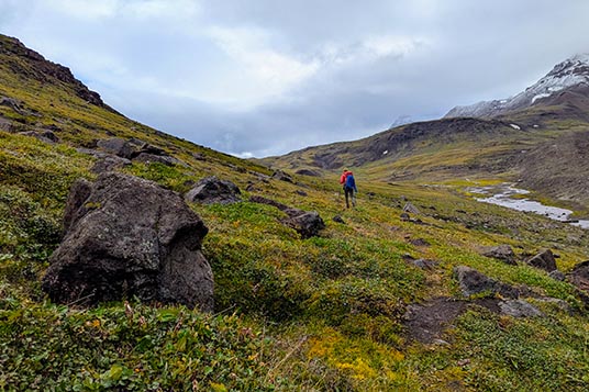 A hiker moves through tundra and boulders in Alaska