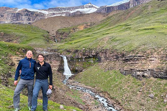 Two men pose in front of a waterfall