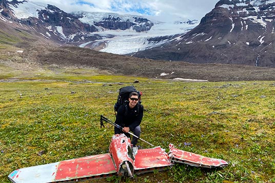 A backpacker kneels next to an tail of an old airplane wreck