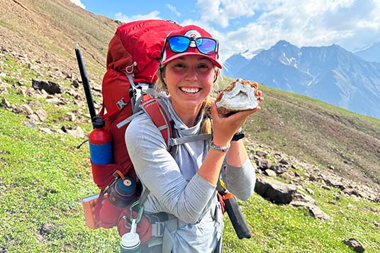 A backpacker smiles at the camera with a large geode in hand