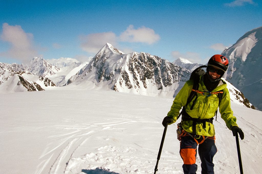 A ski guide in a yellow jacket standing in front of impressive mountains in Wrangell - St. Elias National Park