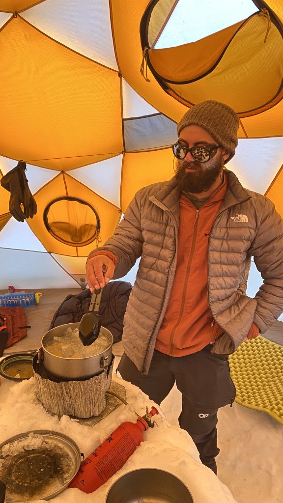 A ski guide melts snow into water while standing comfortably inside a tent