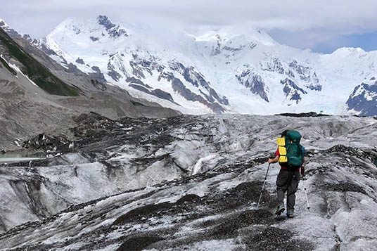 A backpacker on a glacier with views of a cloudy Mt. Blackburn