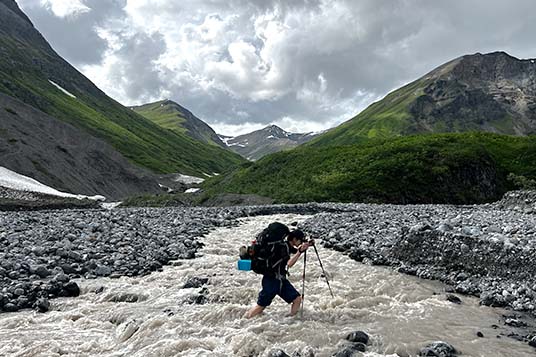 A backpacker crossing a creek in Wrangell - St. Elias National Park