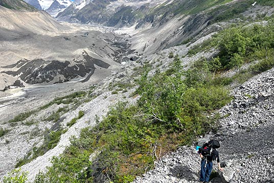 A backpacker navigates rocks and brush in the Wrangell Mountains