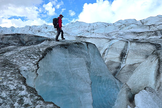 A backpacker stands atop a tall glacial cliff