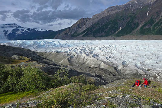 Two hikers at the edge of a glowing white valley glacier in Alaska