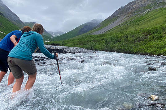 Two women link arms to cross a creek