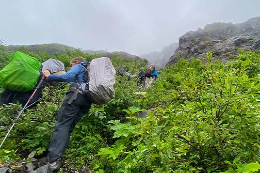 Backpackers heading up a steep and brushy hillside