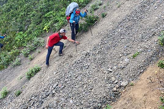 A guide helps a backpacker on a steep slope