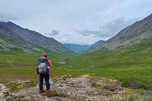 A backpacker takes in the view of a green, tundra-covered mountain valley