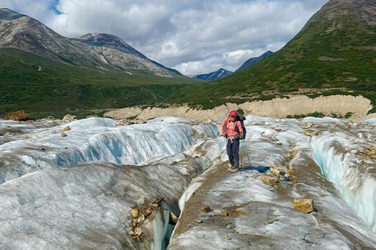 A female backpacker traverses a glacier between crevasses