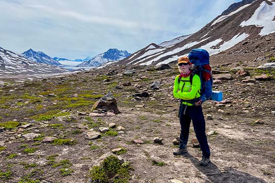 A backpacker in a bright jacket poses in front of a rocky mountain valley