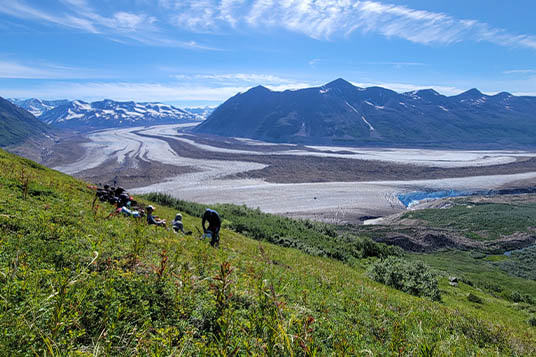 Backpackers take a break on a steep slope overlooking a glacier