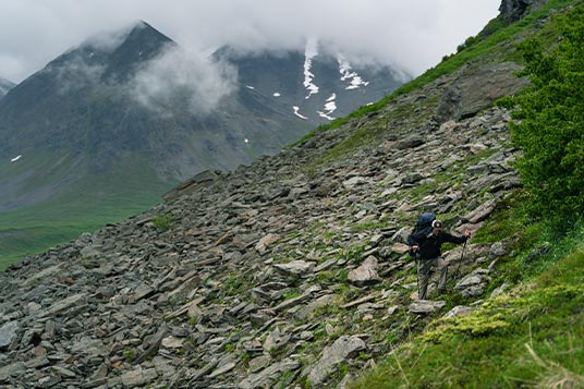 A backpacker traverses a rocky and steep slope in Alaska