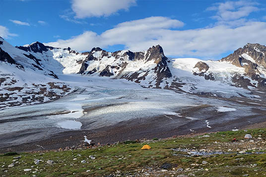 A small yellow tent dwarfed by the glaciated mountains of the Chugach