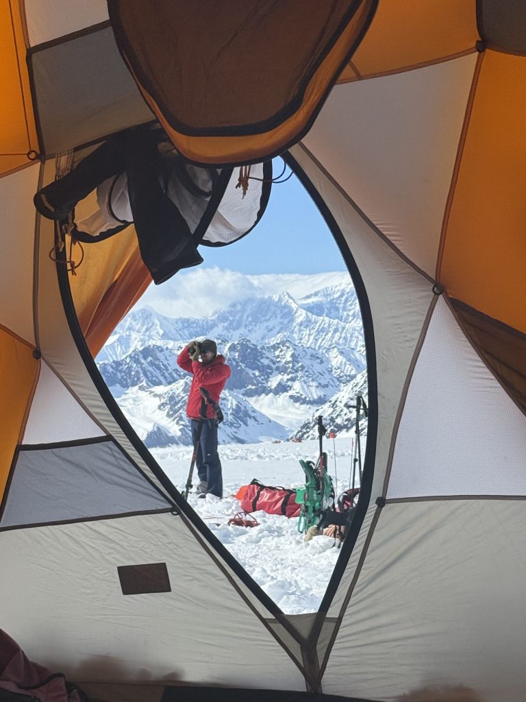A view of a person taking a picture with snowy mountains out of a tent window