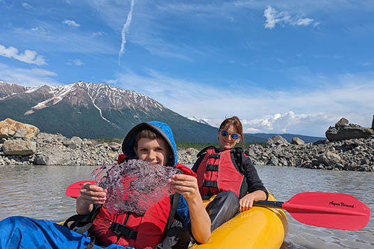 A mother and son in an inflatable kayak in Wrangell - St. Elias National Park. The son is holding a large piece of glacial ice.