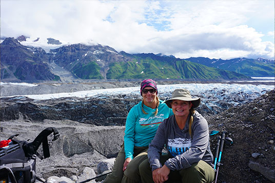 Two female hikers pose in front of a glacier