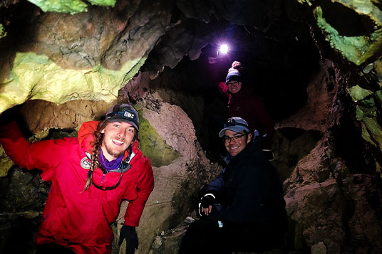 Three people in headlamps in a cave