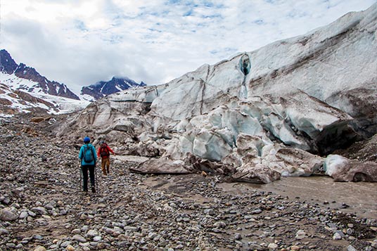 Two hikers approach a big glacial wall