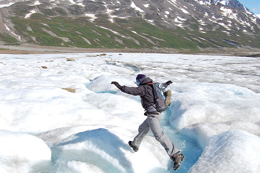 A glacier hiker jumps over a stream on the ice