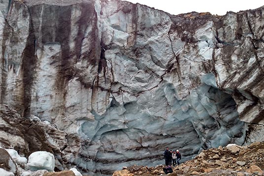 A group of people dwarfed by a giant glacial wall
