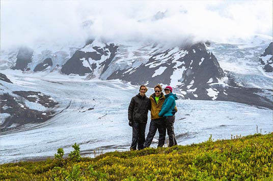 Three friends pose in front of a glacier in Alaska