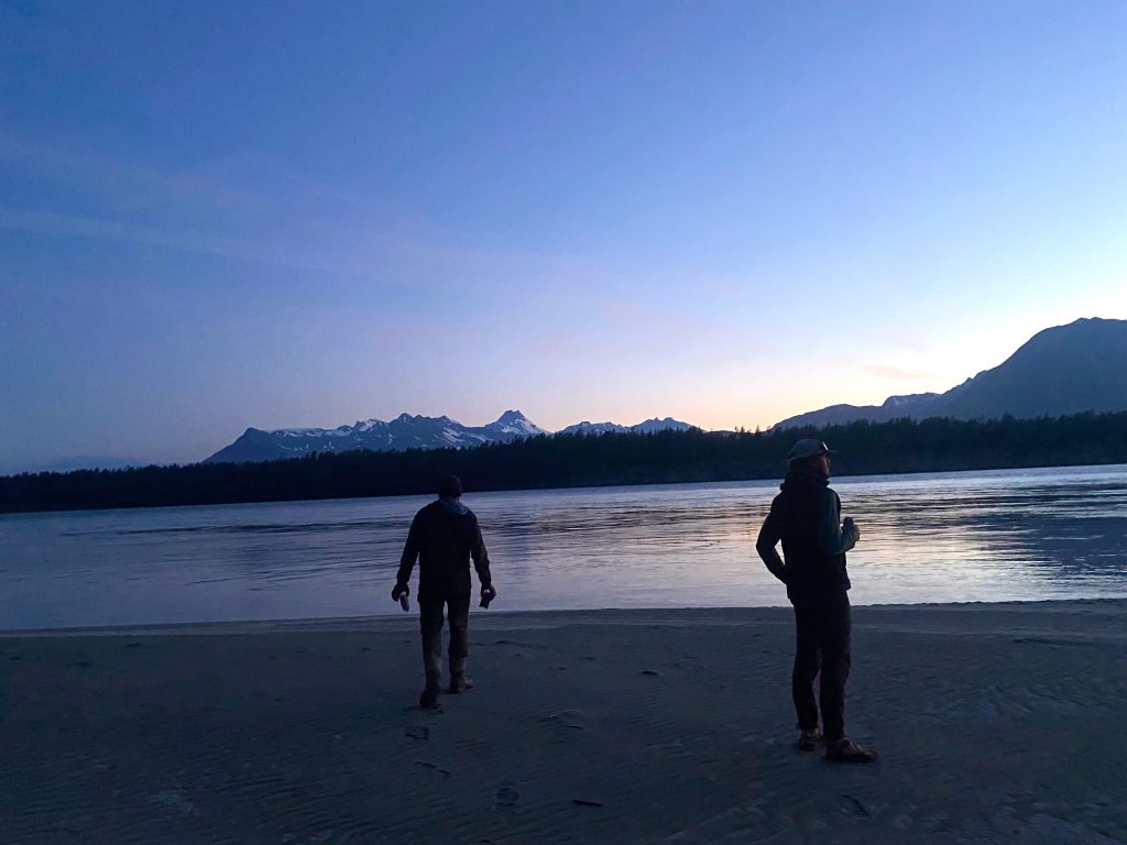 Two raft guides watch the sunset over snowy mountains and the Copper River